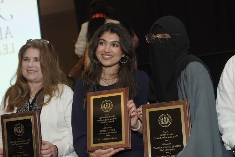 three people stand together holding their award plaques