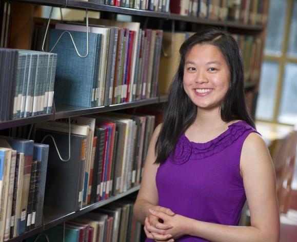 Scholarship winner smiles in library stacks.